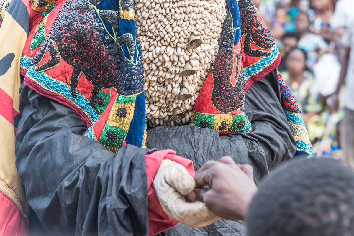 Een gemaskerde man krijgt geld van een toeschouwer tijdens een voodoo ceremonie in Benin