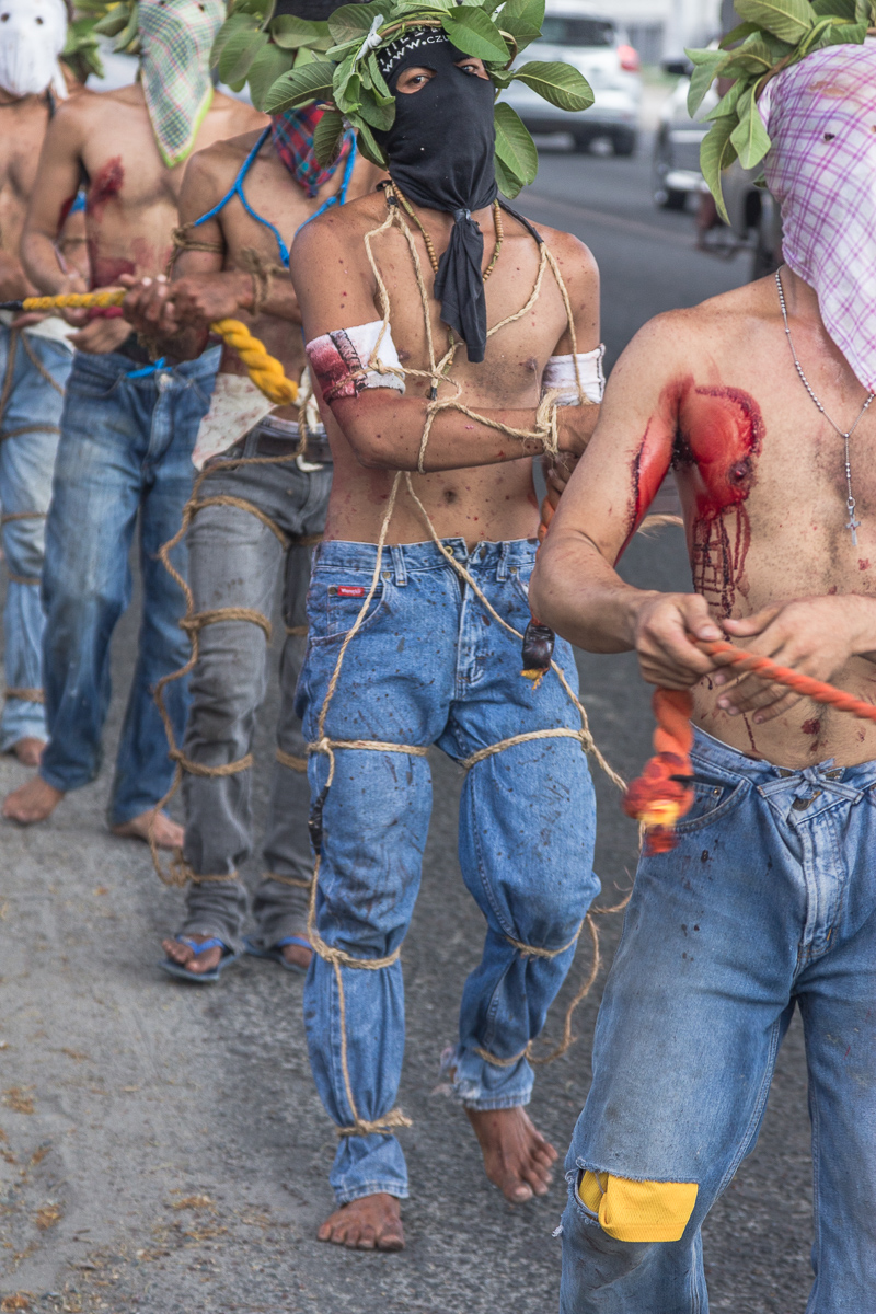 Processie door de straten van Angeles en San Fernando op de Filipijnen, terwijl gemaskerde mannen zichzelf op de rug slaan met houten klossen.